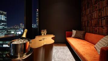 A modern living room with a city view, a bookshelf, and a bar area with a bottle of champagne and glasses.