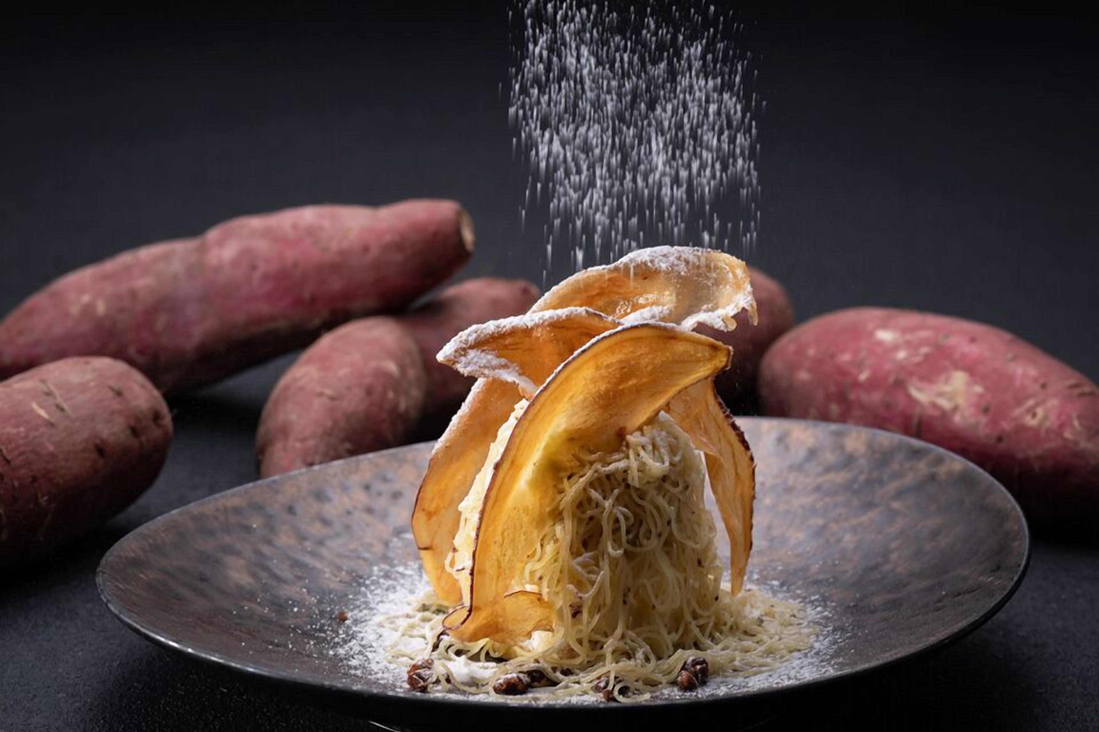 A plate with sliced sweet potatoes and a dusting of white powder, with more whole sweet potatoes in the background.