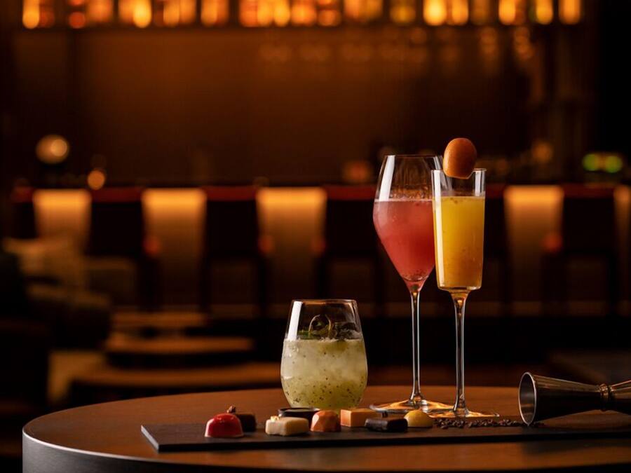 Un bar con dos bebidas: una copa de cóctel y un vaso highball, junto con una copa de martini con un cóctel.