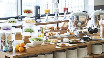 A buffet setup with various food items, including fruits, salads, and bread, arranged on a wooden table with stacked plates and bowls.