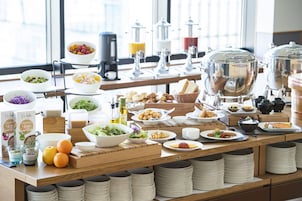 Un buffet proposant une variété de plats, notamment des fruits, des salades et du pain, disposés sur une table en bois avec des assiettes et des bols empilés.