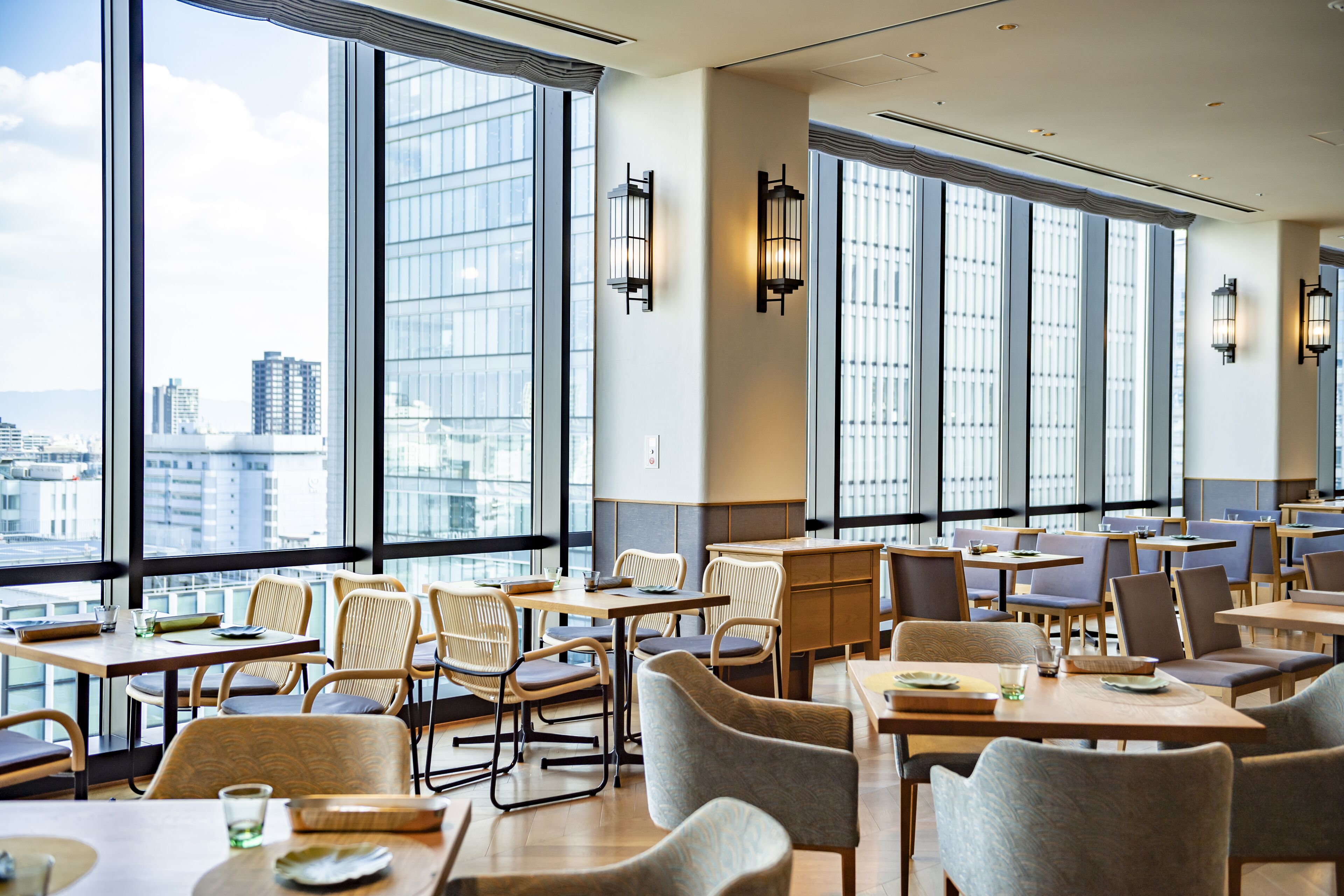 Un comedor moderno con ventanas amplias, mesas y sillas de madera, que ofrece vistas del paisaje urbano.