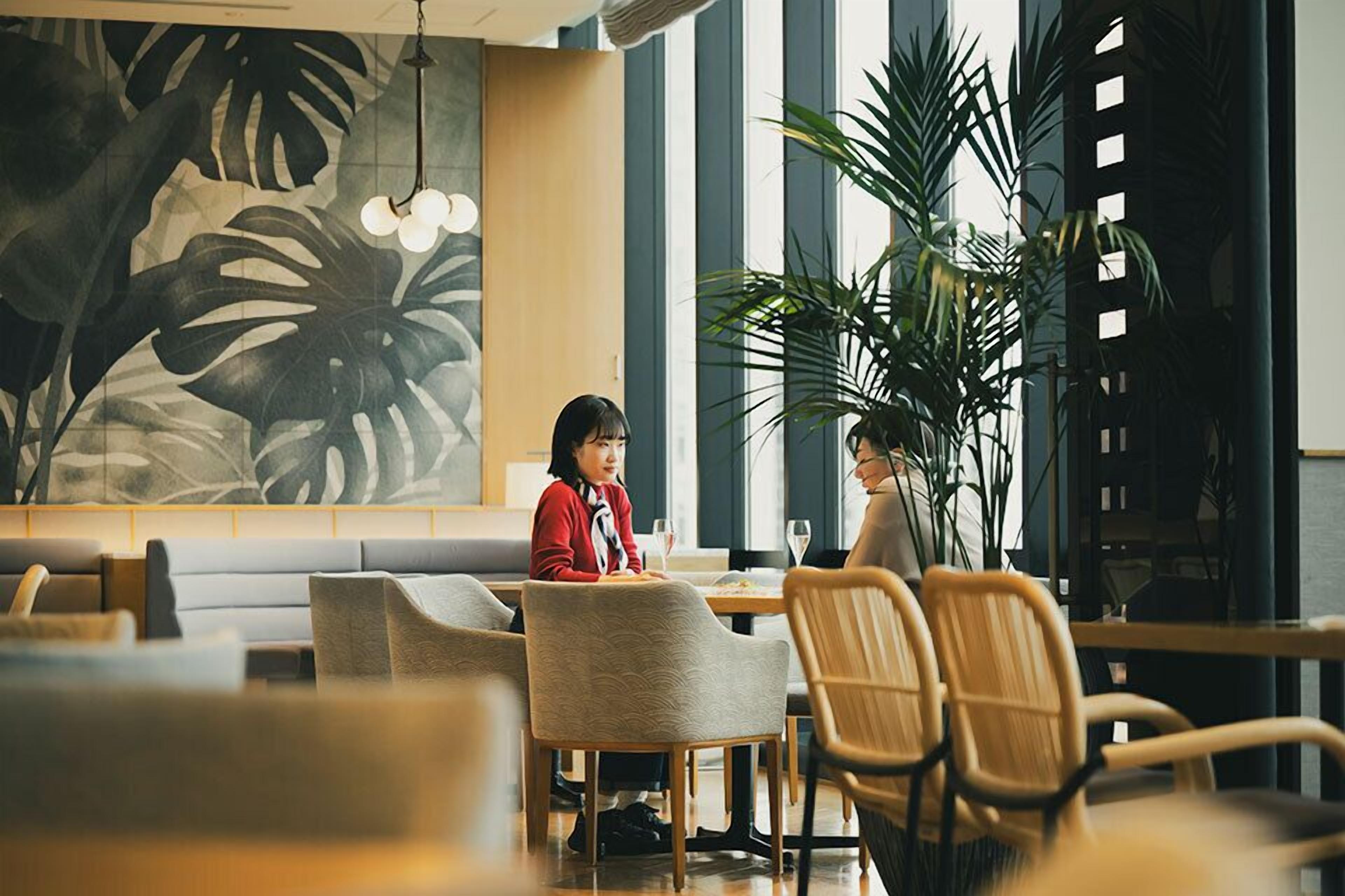 A restaurant with a large leafy plant, wooden tables, and chairs.