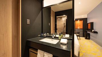A modern bathroom with a large mirror, a sink, and a shower. There is a towel rack and a small table with toiletries.