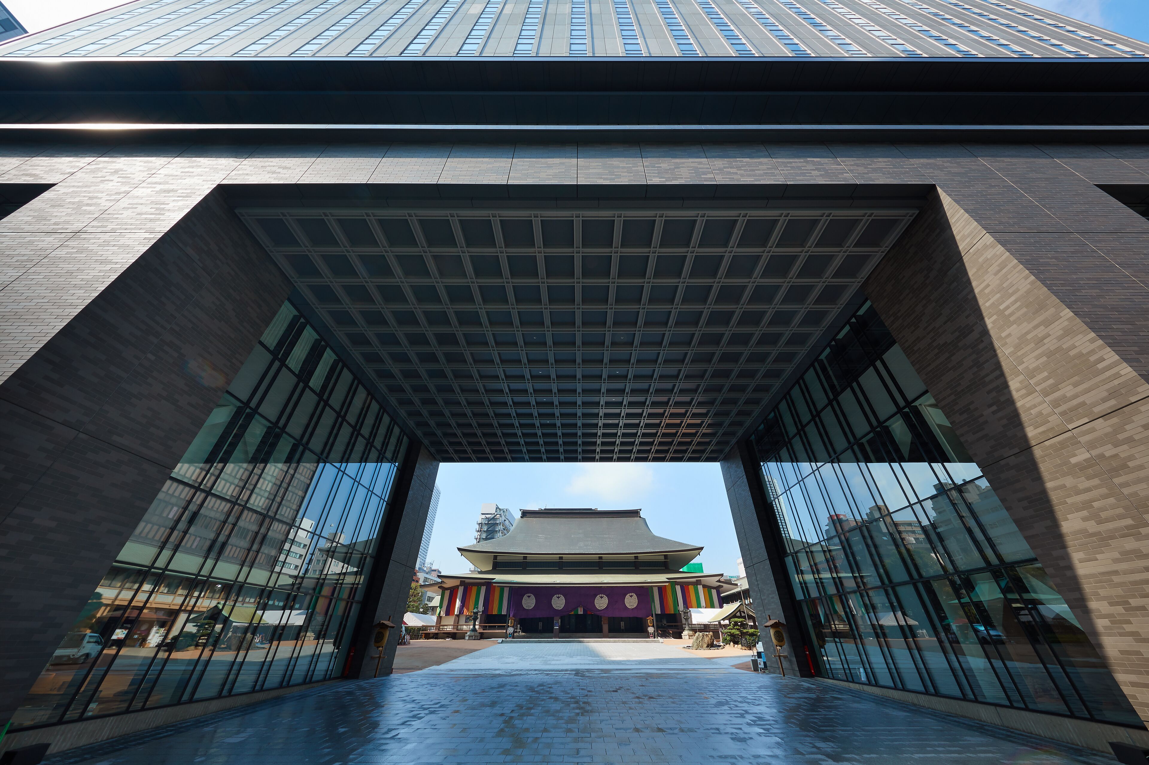 A modern building with a large glass entrance and a traditional structure in the background.