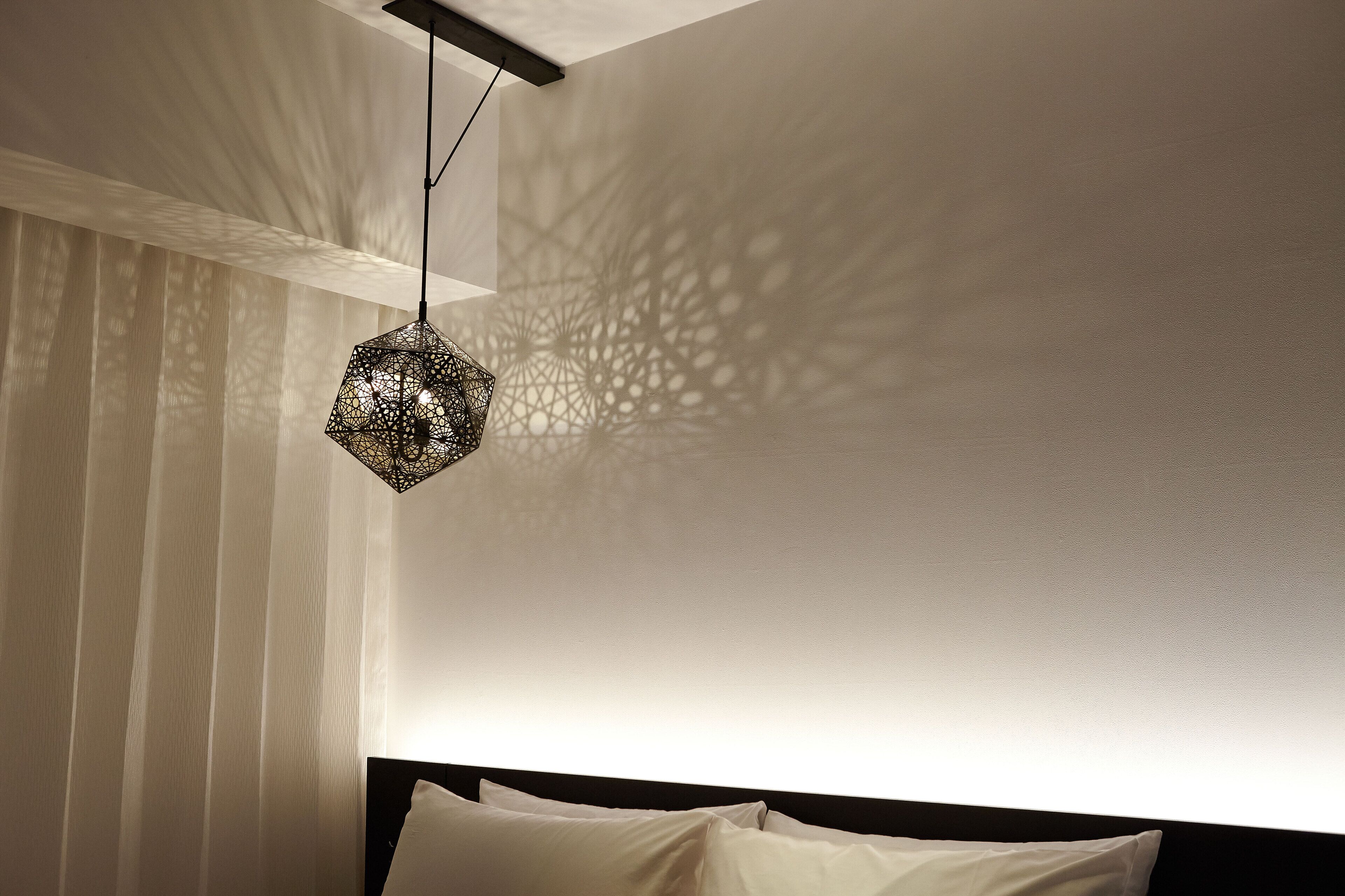 A bedroom with a geometric patterned light fixture casting intricate shadows on the wall.