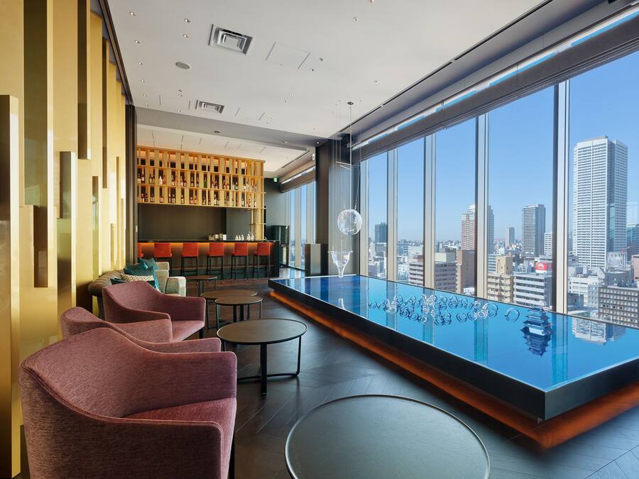 Un salon moderne doté d’une piscine à débordement en verre, de coins salon et offrant une vue sur la ville.