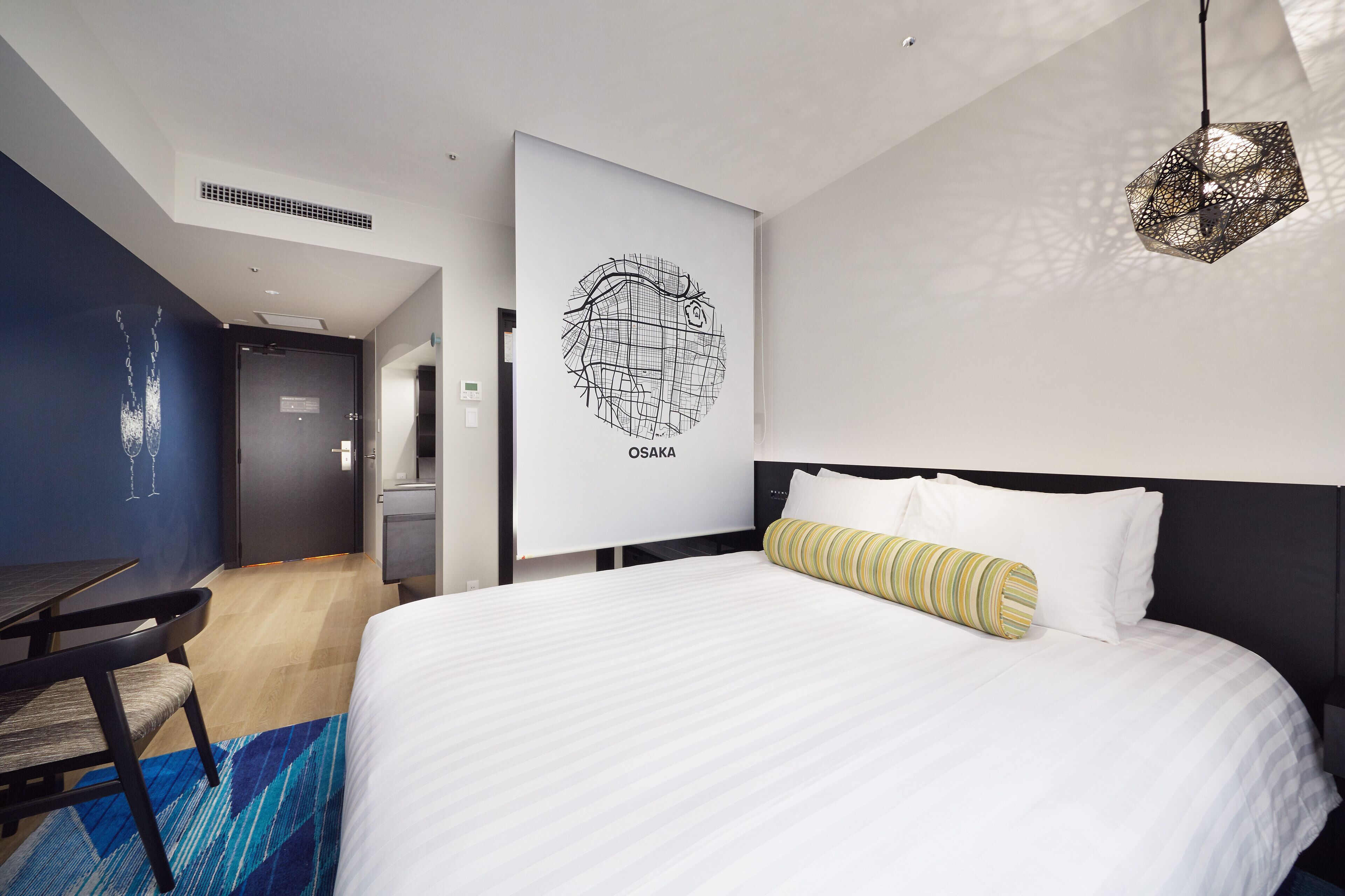 A modern hotel room with a large bed, a desk, and a wall-mounted artwork labeled "OSAKA".