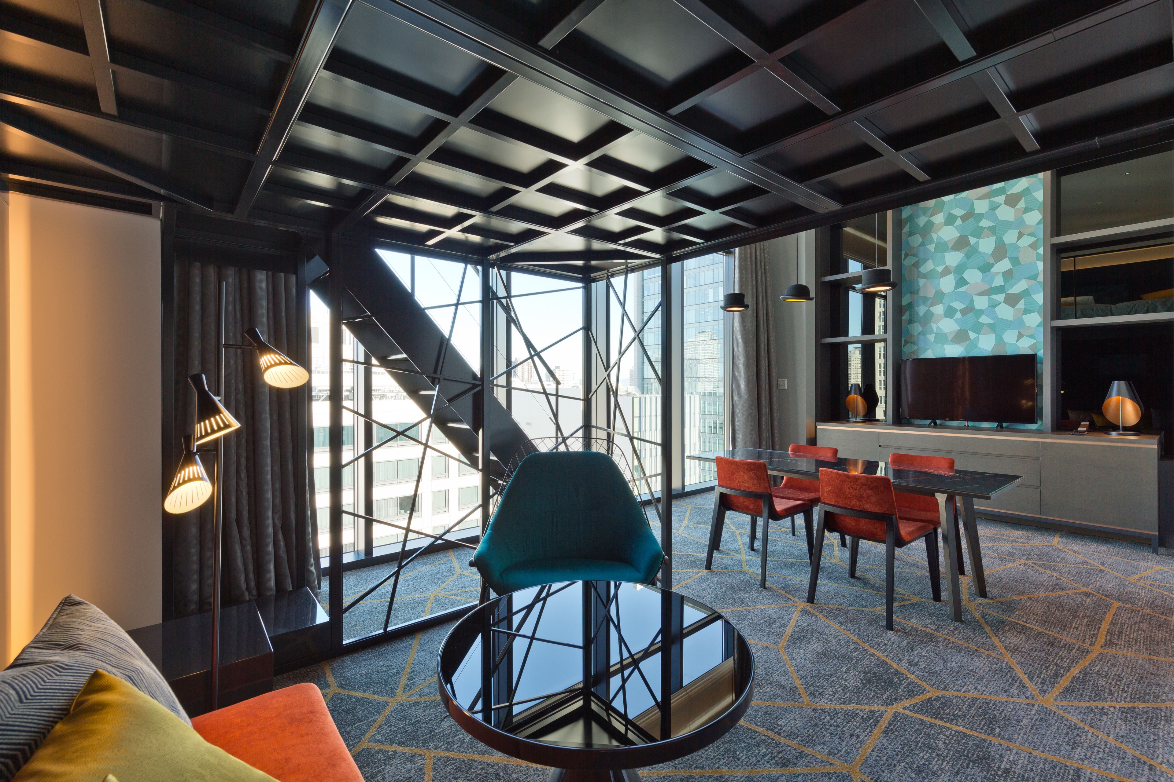 A modern hotel room with a large window, a round table with chairs, and a sofa.