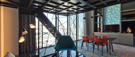 A modern hotel room with a large window, a round table with chairs, and a sofa.