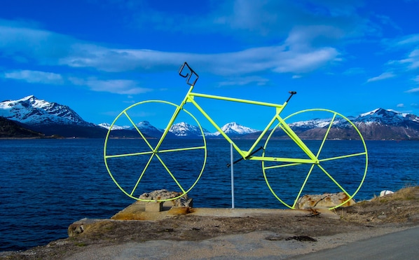 A bicycle with a bright yellow frame and black handlebars, positioned on a concrete platform by a body of water with mountains in the background. - Lofoten Gate Hostel (Lødingen)