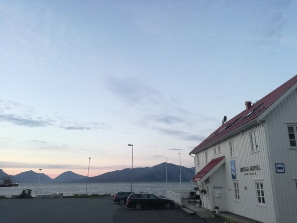 A white building with a red roof, labeled "Bygga Hotel," adjacent to a body of water with mountains in the background. - Lofoten Gate Hostel (Lødingen)