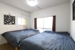 A bedroom with two single beds, a window with curtains, and a decorative wall piece. - Simon's house Shinjuku (Tokyo)