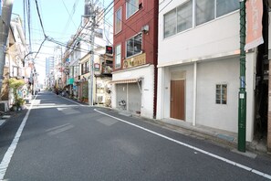A narrow urban street lined with multi-story buildings, some with visible commercial signage. - Simon's house Shinjuku (Tokyo)