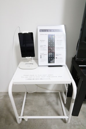 A white table with a tablet and a remote control, a sign with instructions, and a cable management system. - Simon's house Shinjuku (Tokyo)