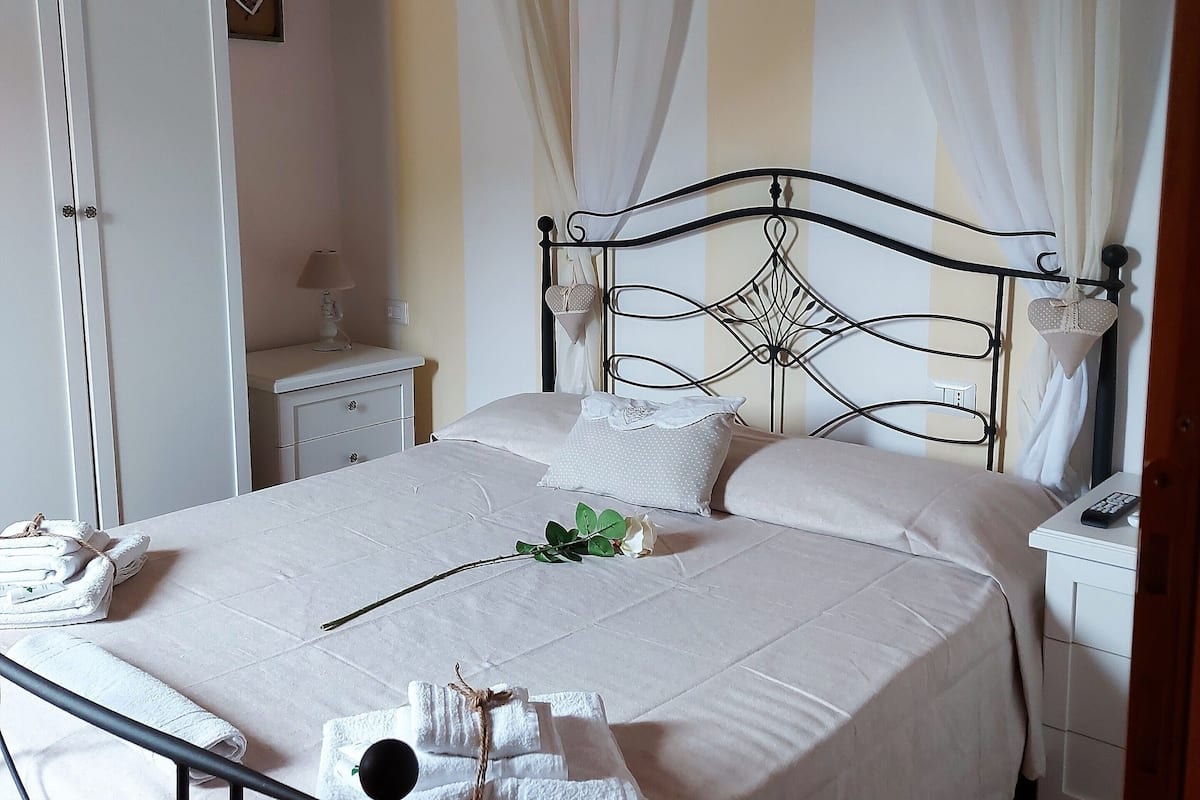 A neatly made bed with white linens, a bedside table with a lamp, and a wardrobe.