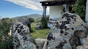 A rustic stone house with a tiled roof, surrounded by large rocks and greenery, overlooking a mountainous landscape. - B&B Su Donnigheddu (Golfo Aranci)