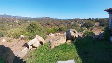 Vista de un paisaje rural con una construcción de piedra, una zona de césped y una cadena montañosa distante.