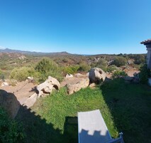 Vista de un paisaje rural con una construcción de piedra, una zona de césped y una cadena montañosa distante.