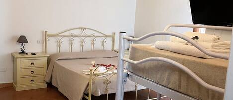 Un dormitorio con una cama doble, una mesita de noche con lámpara, una cama con cubrecama blanco y un equipo de aire acondicionado en la pared.