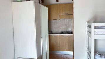 A bedroom with a bed, a white wardrobe, and a small kitchenette with a tiled backsplash and wooden cabinets.