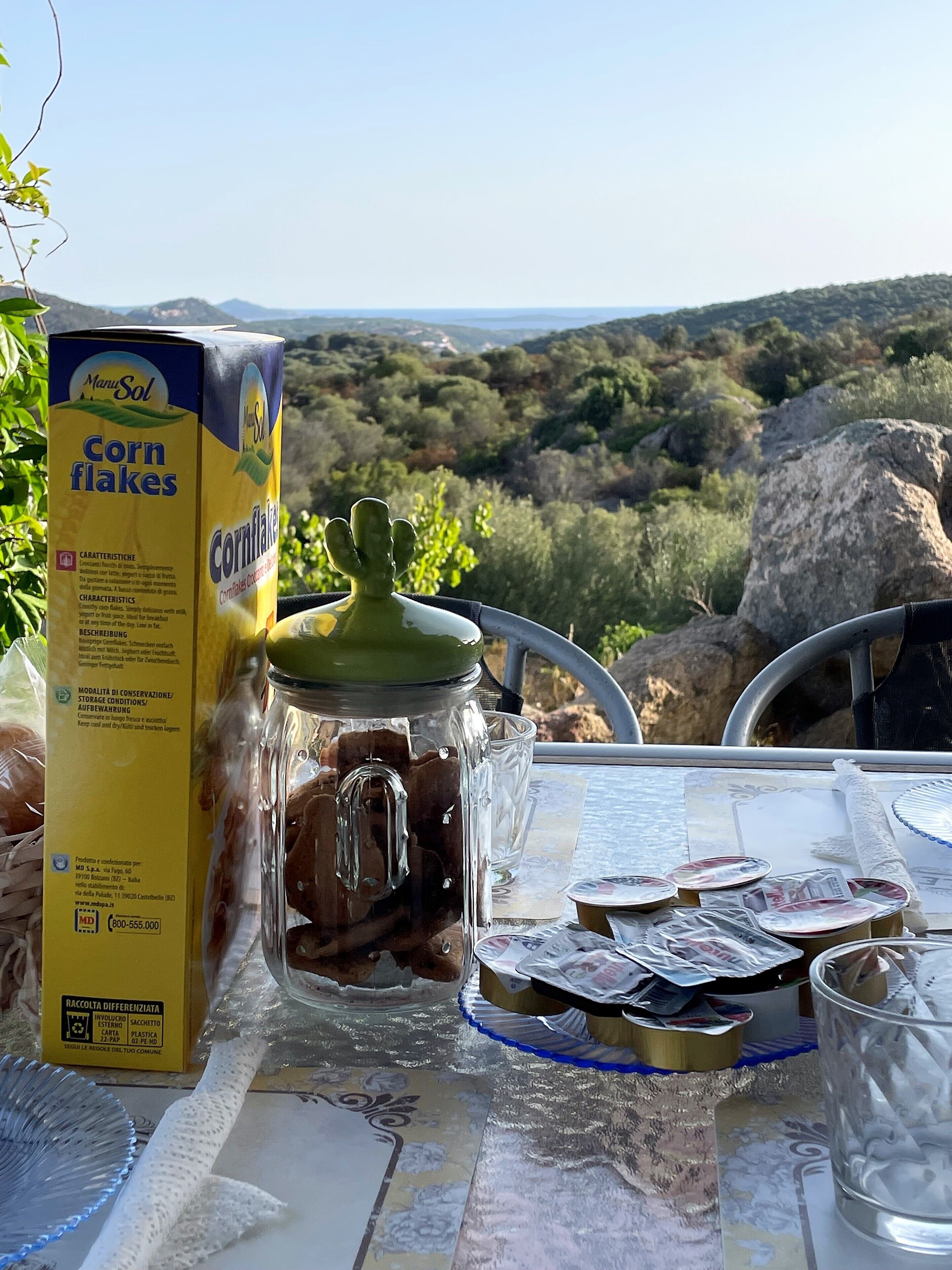 Uma mesa com uma caixa de flocos de milho, um pote de vidro e alguns alimentos embalados.