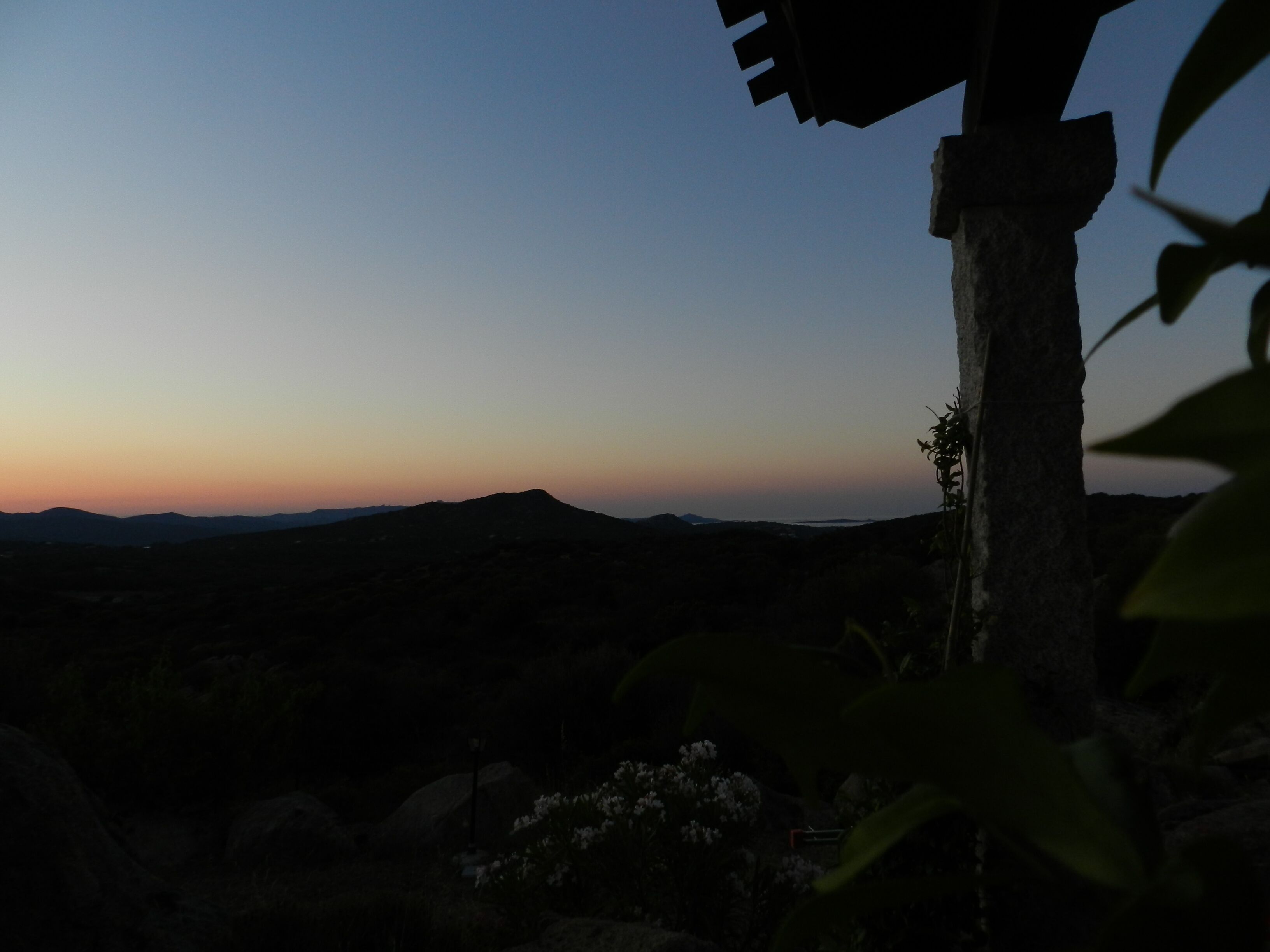 Vista de uma paisagem montanhosa ao entardecer, com o perfil de uma construção em primeiro plano.