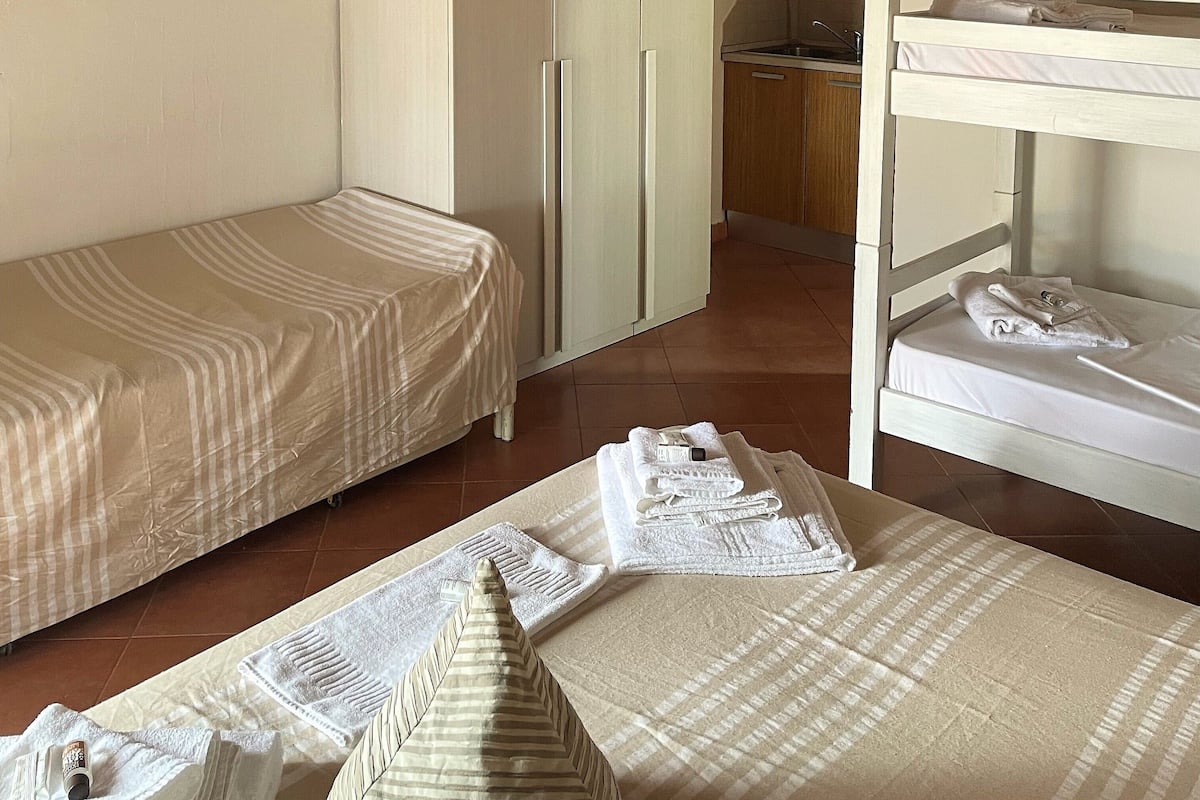 A small, cozy room with a bunk bed, a single bed, a wardrobe, and a kitchenette.