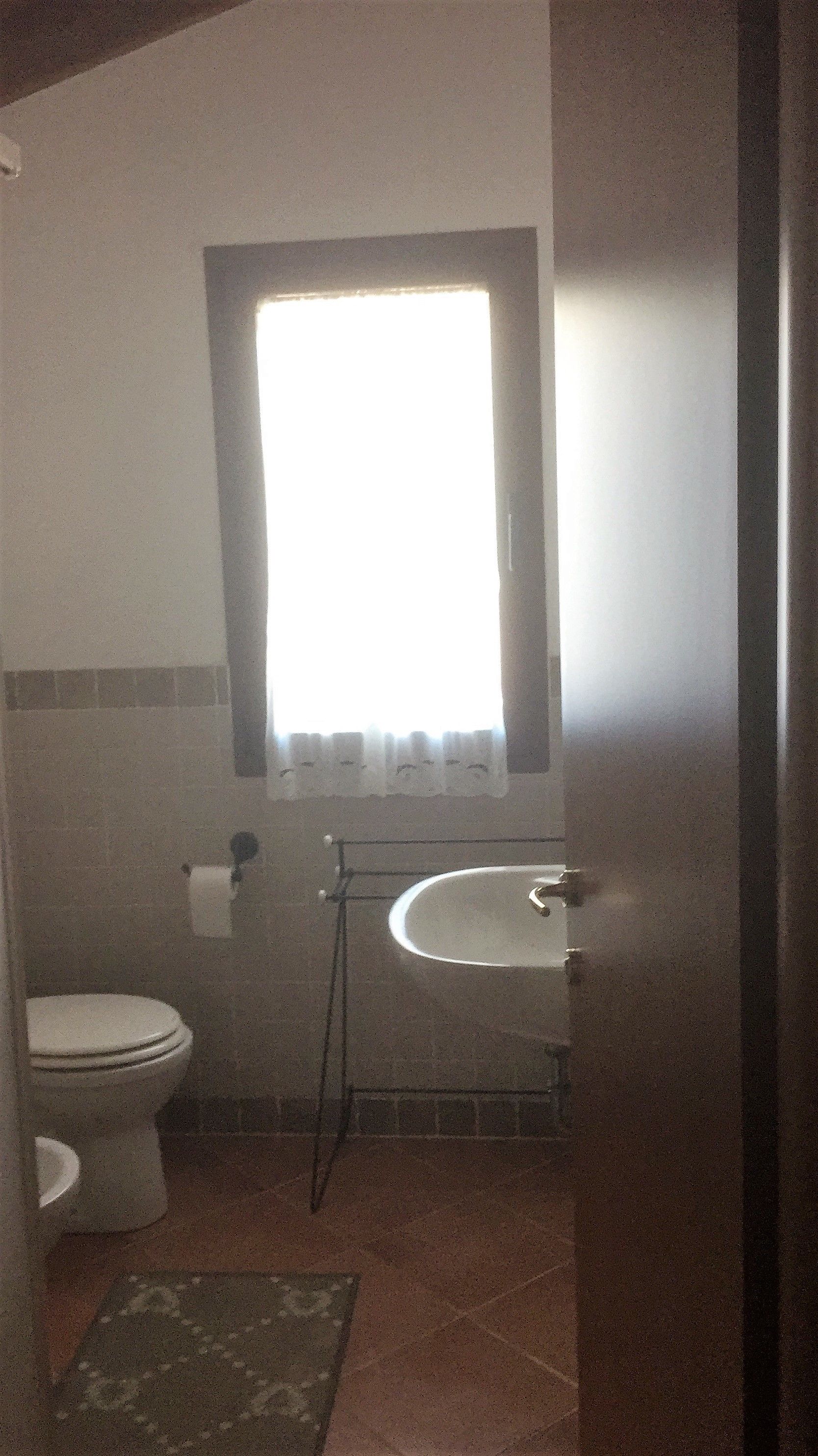 Un baño pequeño con inodoro, lavamanos y una ventana sobre el lavamanos.