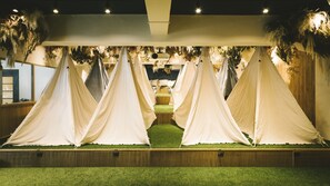 A room with four white tents arranged in a row, each with a wooden platform and green artificial grass. - Theater Zzz - Hostel (Tokyo)