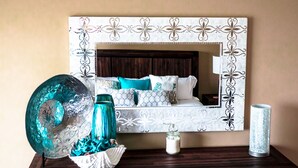 Un dormitorio con cama, almohadones decorativos, una gran escultura de cristal y una vela sobre una mesita de noche de madera.