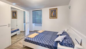 A bedroom with a bed, a wardrobe, a window with blinds, and two paintings on the wall. - Apartment Old City 1 (Pula)