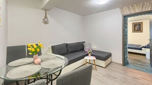 A modern living room with a grey sofa, a glass coffee table, and a small round table with a vase of flowers. - Apartment Old City 1 (Pula)