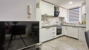 A modern kitchen with white cabinets, a marble backsplash, a built-in oven, and a large flat-screen TV. - Apartment Old City 1 (Pula)