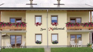 Ein zweistöckiges Gebäude mit Balkonen, die mit Blumen geschmückt sind, und der Schriftzug „Zum Mühltal