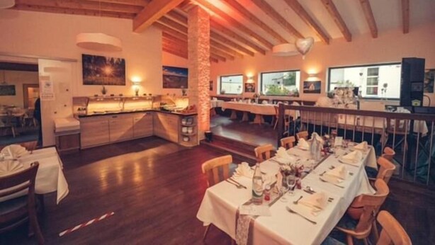 Ein Restaurant mit Holzbalken, einem langen Esstisch, der für eine Mahlzeit gedeckt ist, und einer Bar.