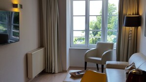 A modern living room with a wooden ceiling, a large window, a sofa, a dining table, and a flat-screen TV mounted on the wall. - Winzerhäusle Meersburg (Meersburg)
