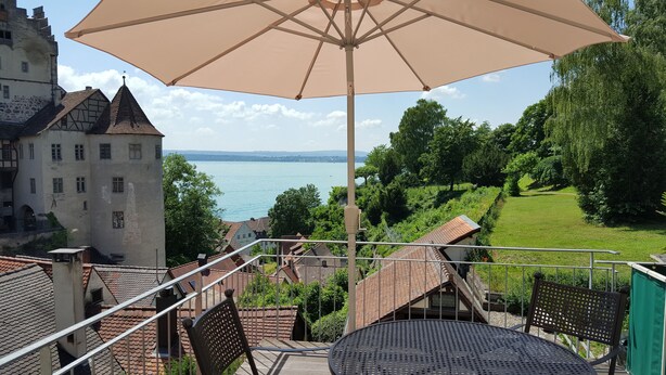 A balcony with a table and chairs, overlooking a lake and a castle. - Winzerhäusle Meersburg (Meersburg)