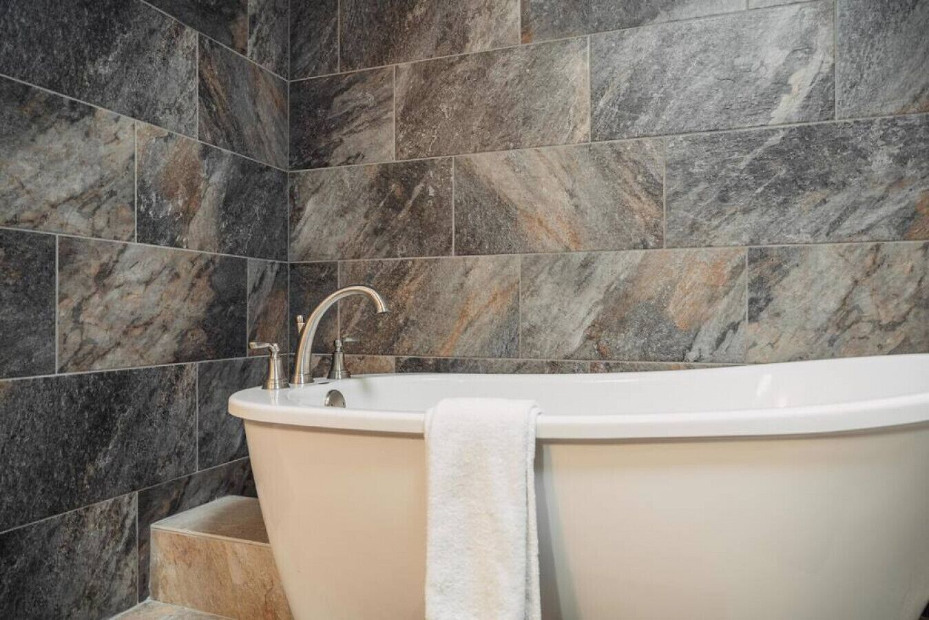 A modern bathroom with a freestanding bathtub, marble tiles, and a towel hanging on the side.