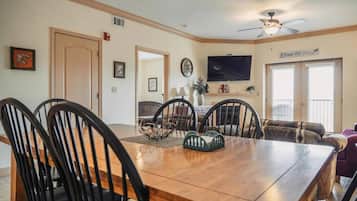 A dining area with a wooden table and chairs, a television mounted on the wall, and a sign that reads "Count Your Blessings".