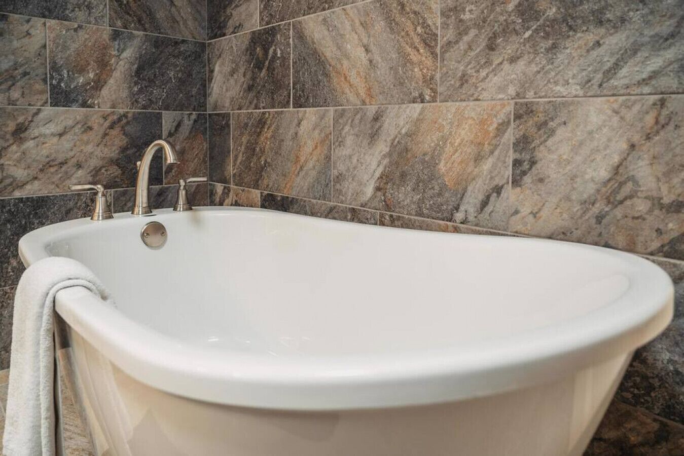 A freestanding bathtub with a single faucet, set against a backdrop of dark, marble-like tiles.