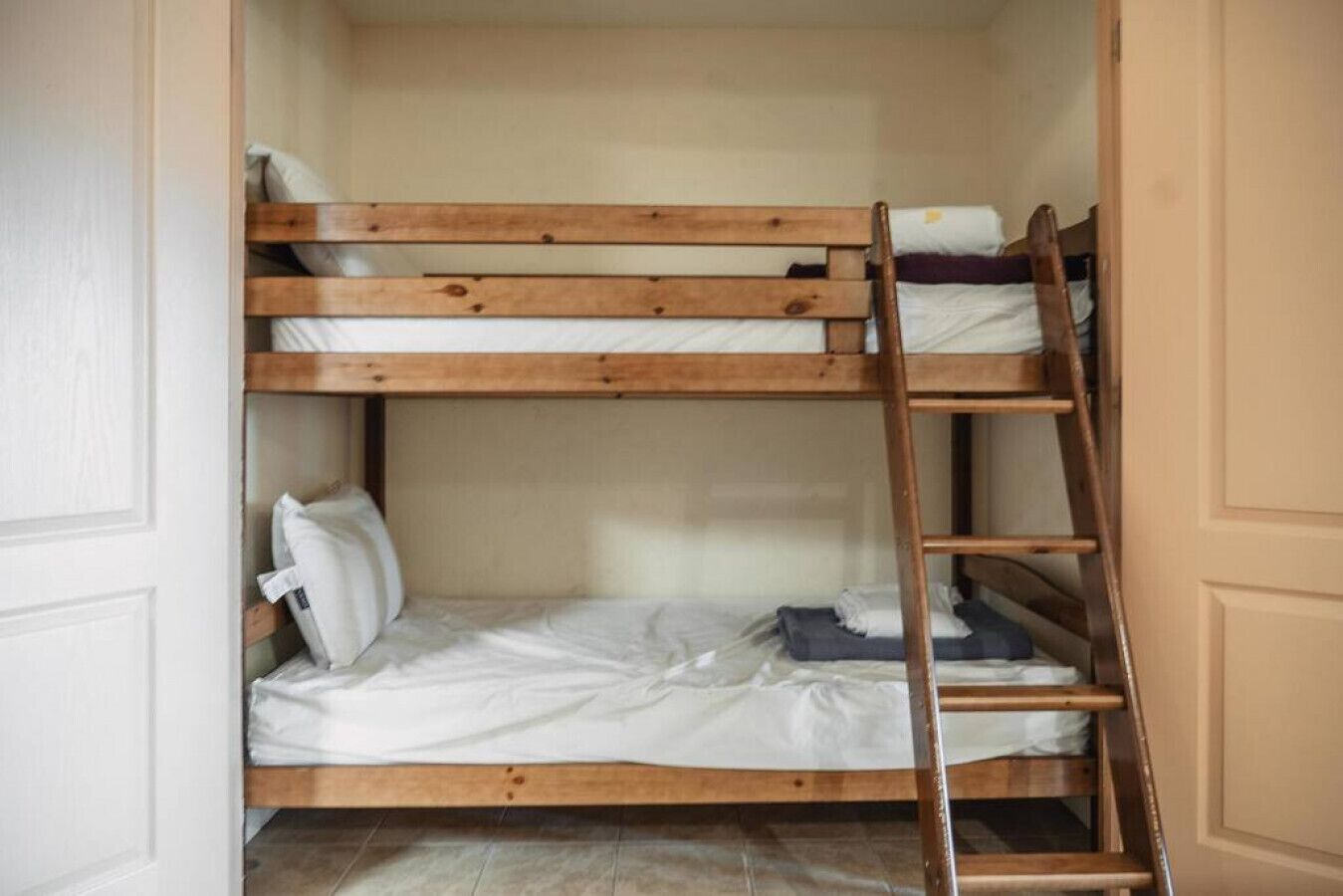 Ein Stockbett mit Holzleiter, weißer Bettwäsche und Fliesenboden.