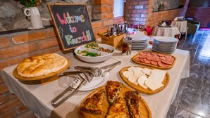 Taula de buffet amb diferents aliments, com ara pizza, amanida i làmines de carn, amb un fons de pared de rajola.