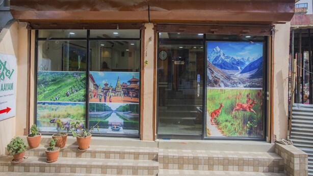 Un bâtiment avec un toit recouvert de tuiles, une entrée en verre ornée d’une affiche et des plantes en pot disposées sur les marches.