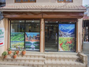 A building with a tiled roof, a glass entrance with a poster, and potted plants on the steps. - OYO 297 Hotel Aayam (Kathmandu)