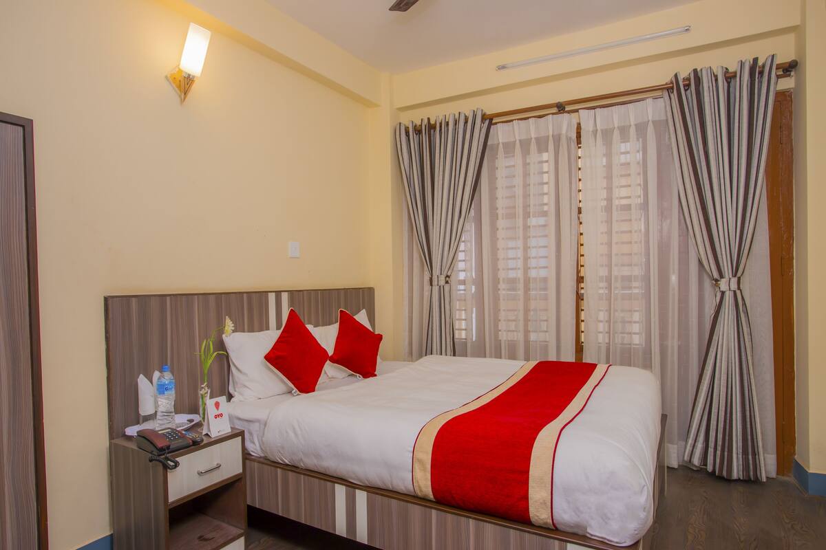 A hotel room with a bed, a nightstand, a lamp, and curtains.