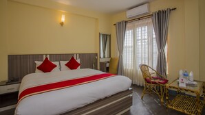 Une chambre d’hôtel avec un grand lit, une table de chevet, une chaise, une petite table avec une bouteille et un appareil de climatisation.