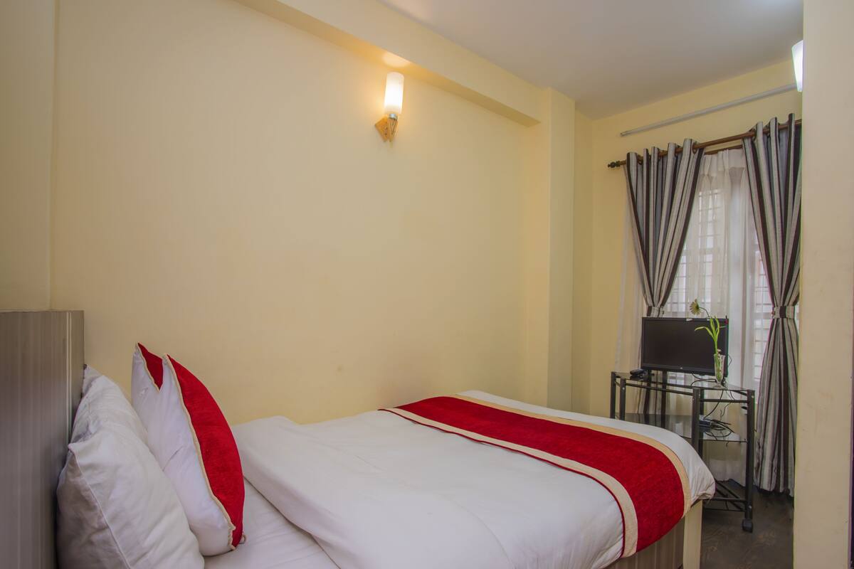 A hotel room with a bed, a desk, a chair, a TV, and curtains.