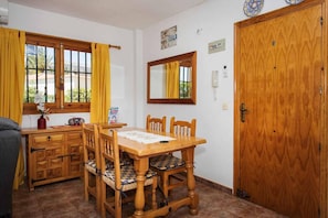 A room with a wooden dining table, chairs, a mirror, a wooden wardrobe, and a window with curtains.