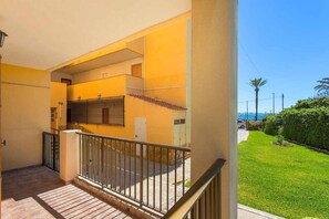 A balcony with a metal railing, a tiled floor, and a view of a green lawn and palm trees.